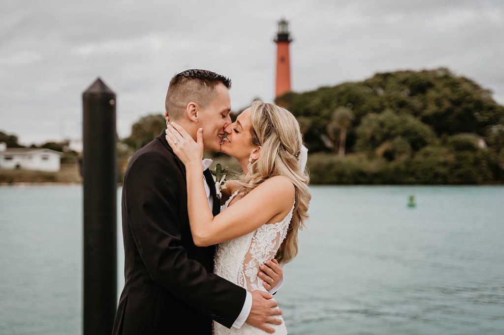 Bride and Groom kissing by the ocean with lighthouse behind them Pelican Club Wedding Photography captured by South Florida Wedding Photographer Krystal Capone Photography