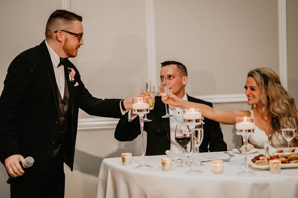 Best man cheering Bride and Groom at sweetheart table Pelican Club Wedding Photography captured by South Florida Wedding Photographer Krystal Capone Photography