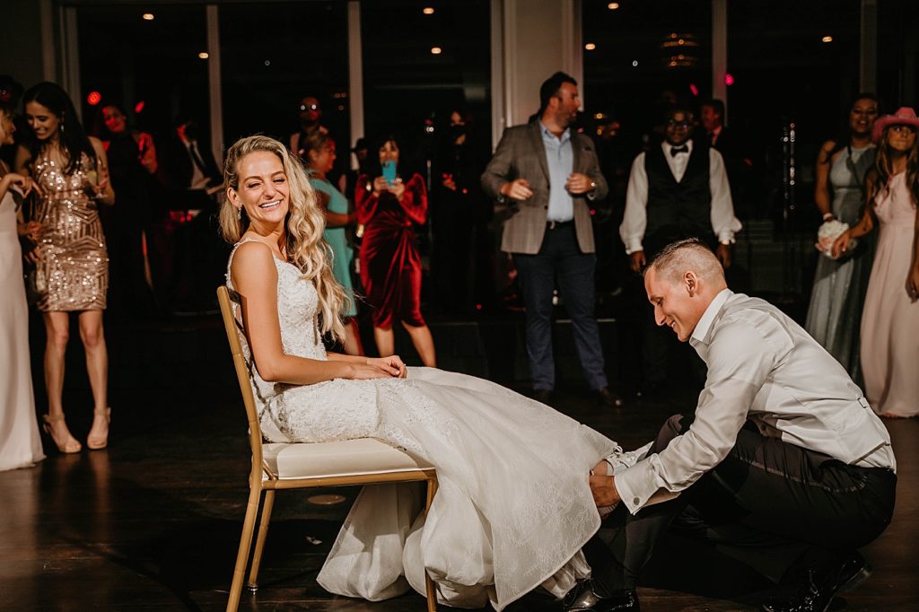 Bride sitting while Groom retrieves garter Pelican Club Wedding Photography captured by South Florida Wedding Photographer Krystal Capone Photography