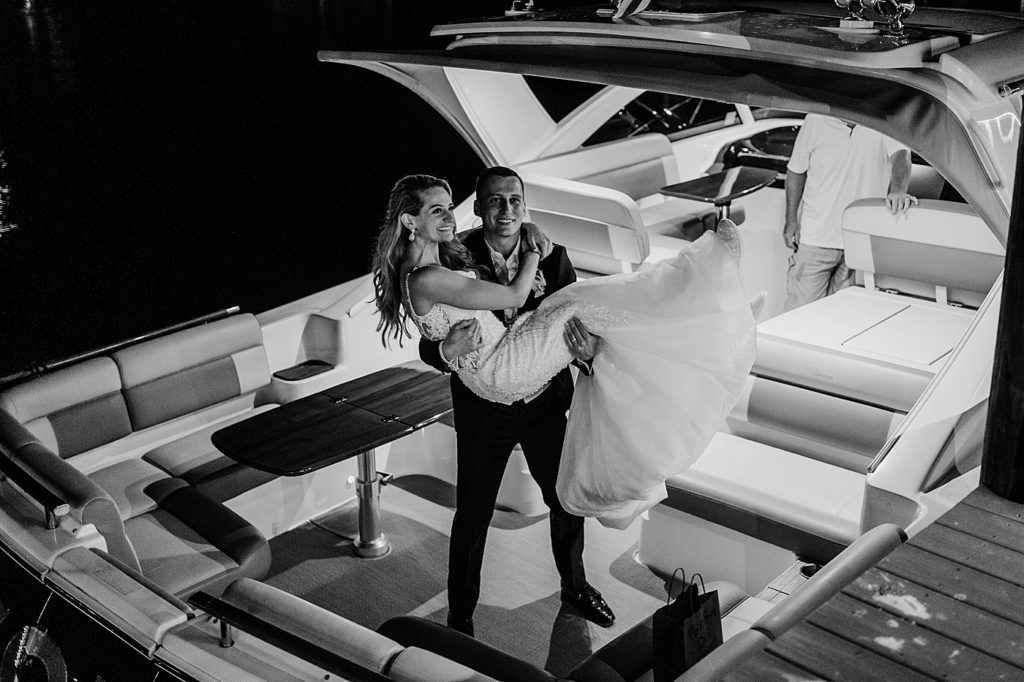 Groom carrying Bride onto boat B&W Pelican Club Wedding Photography captured by South Florida Wedding Photographer Krystal Capone Photography