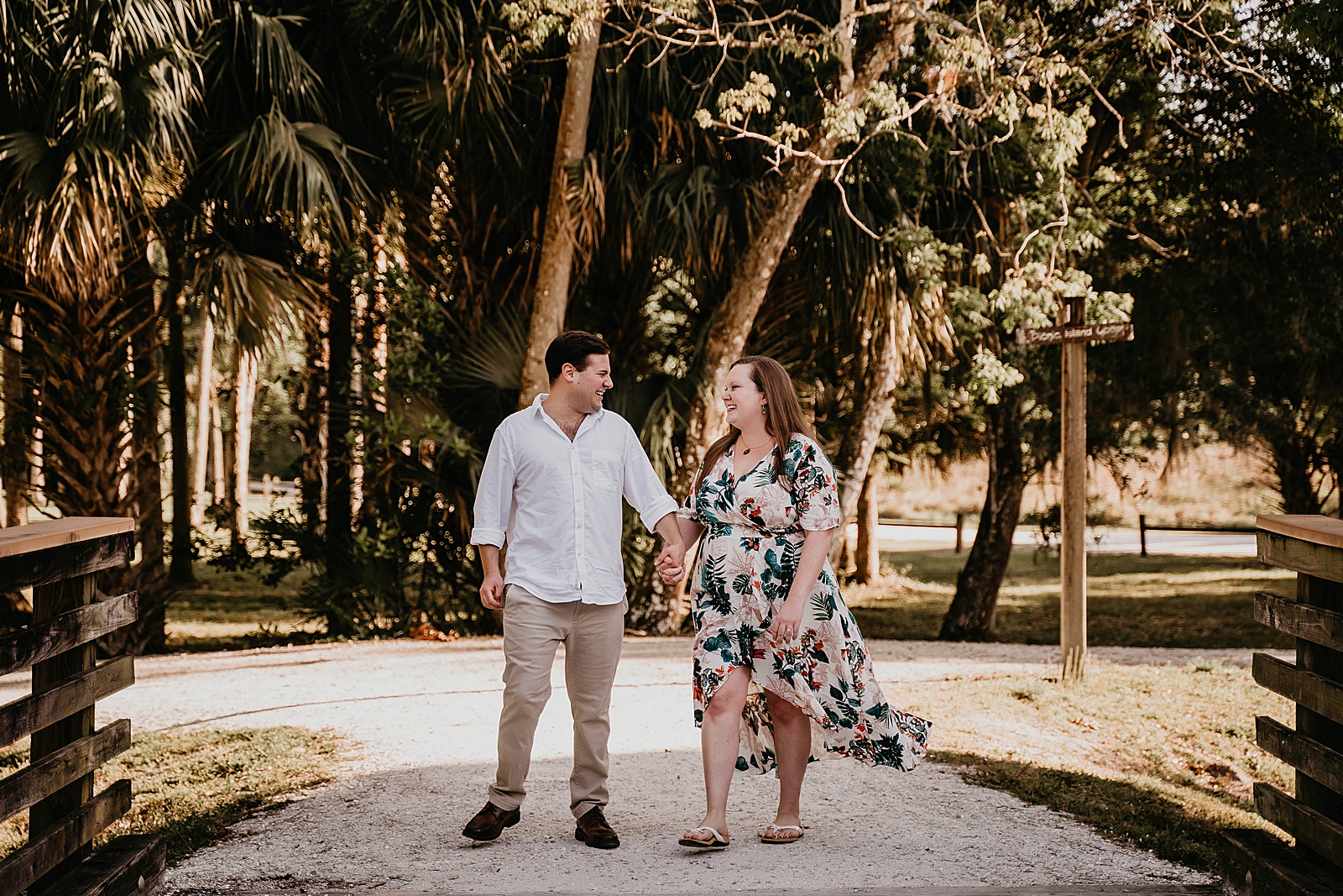 Couple holding hands laughing as they walk onto a bridge Riverbend Park Engagement Photography captured by South Florida Engagement Photographer Krystal Capone Photography 