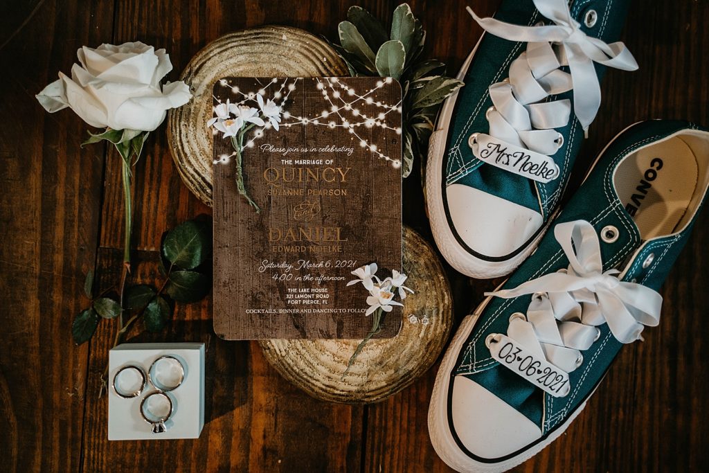 Detail shot of invitation wedding bands wedding rings and white rose and personalized Bridal green converse sneakers with name and wedding date on shoes The Lake House Fort Pierce Wedding Photography captured by South Florida Wedding Photographer Krystal Capone Photography 