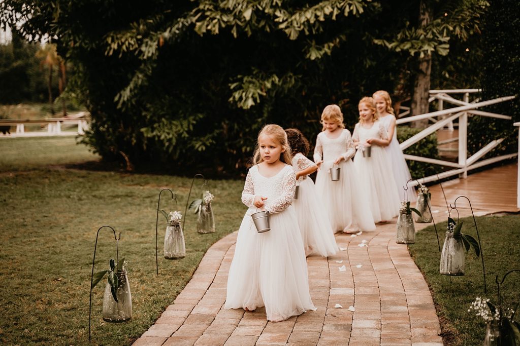 Cute flower girls throwing flower pedals down the stone path Ceremony The Lake House Fort Pierce Wedding Photography captured by South Florida Wedding Photographer Krystal Capone Photography 