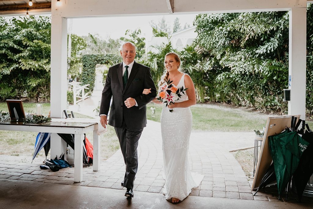 Father and Bride entering Ceremony arm in arm with orange tropical bouquet The Lake House Fort Pierce Wedding Photography captured by South Florida Wedding Photographer Krystal Capone Photography 