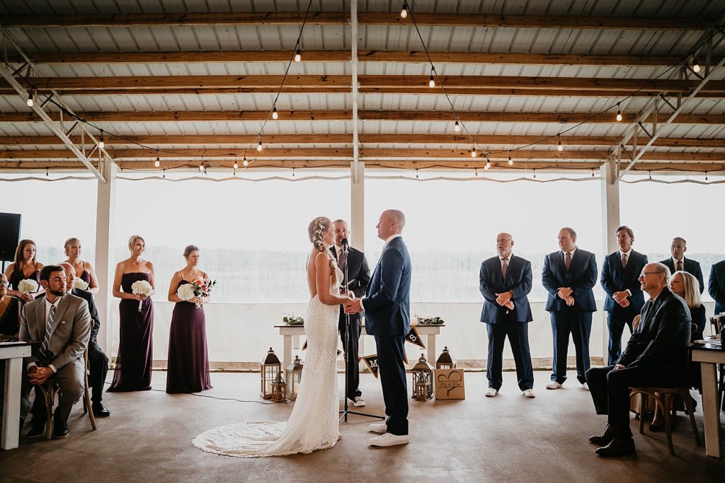 Bride and Groom hand in hand during Homily with Groomsmen and Bridesmaids in formation The Lake House Fort Pierce Wedding Photography captured by South Florida Wedding Photographer Krystal Capone Photography 
