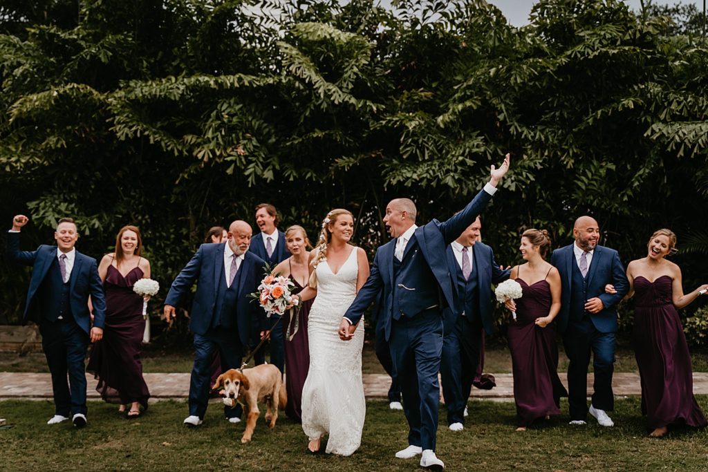 Bride and Groom holding hands with Groom celebrating with rest of Bridal party celebrating The Lake House Fort Pierce Wedding Photography captured by South Florida Wedding Photographer Krystal Capone Photography 