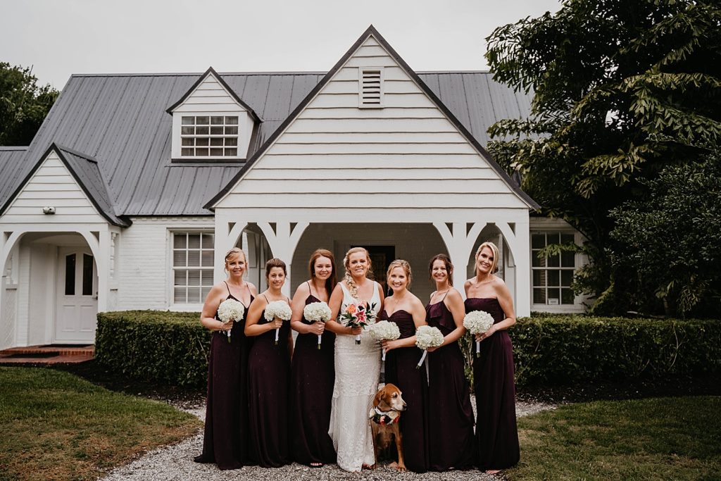 Bride holding tropical bouquet standing with dog and Bridesmaids standing with white bouquet The Lake House Fort Pierce Wedding Photography captured by South Florida Wedding Photographer Krystal Capone Photography 