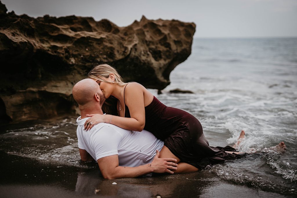 Woman kissing man laying on the wet sand