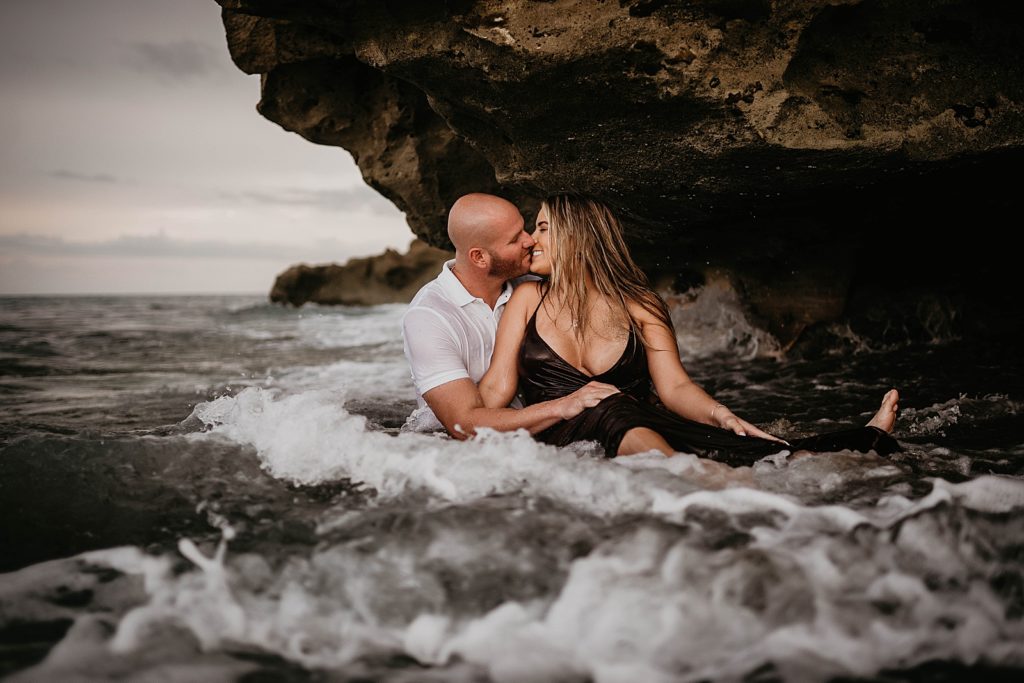 Couple kissing under beach rock in the ocean water