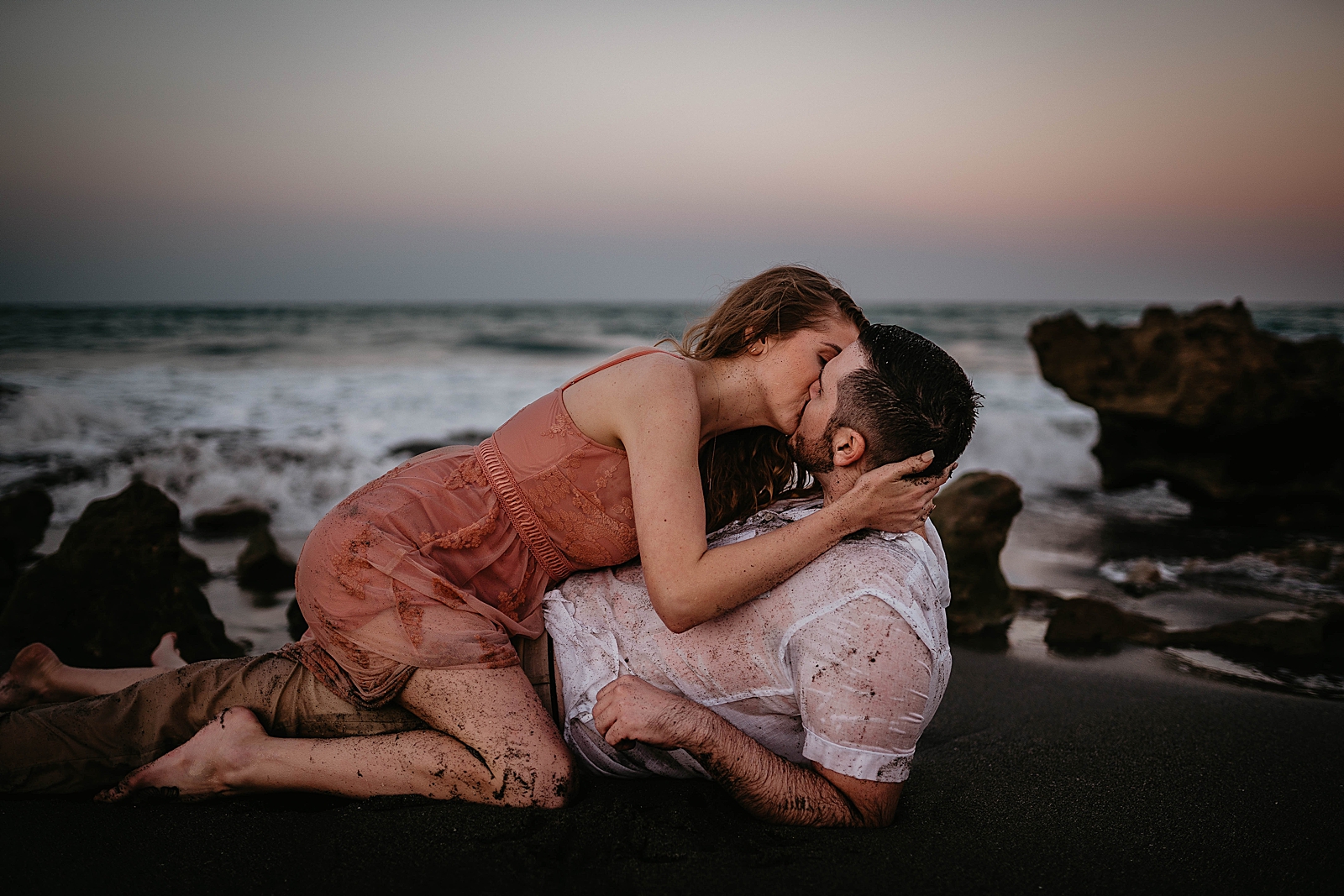Woman kissing man laying on the sand wet