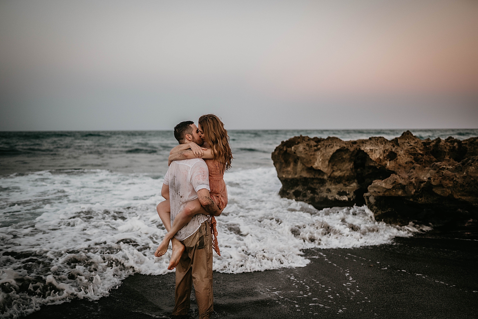 Man holding lady and kissing with waves crashing into them