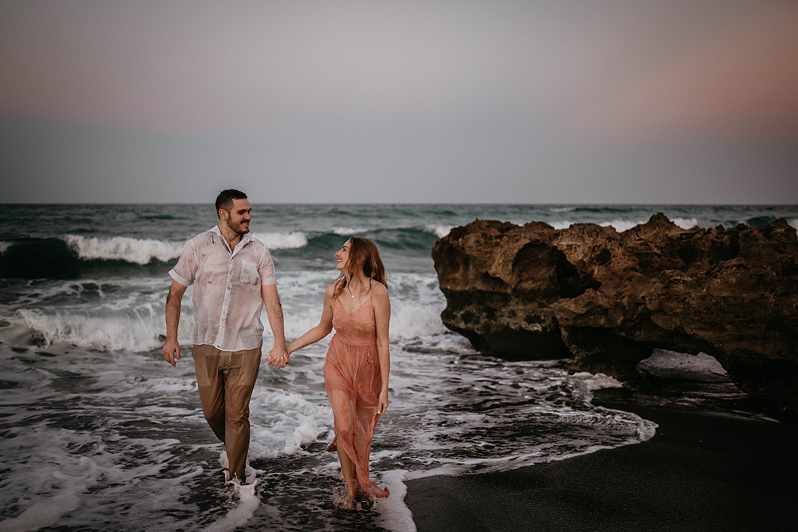 Couple holding hands walking on the on the shallow ocean beach water