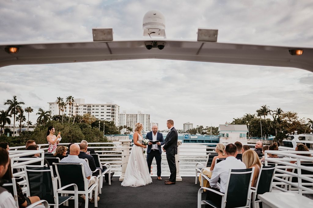 Bride and Groom listening to Homily outside by yachts
