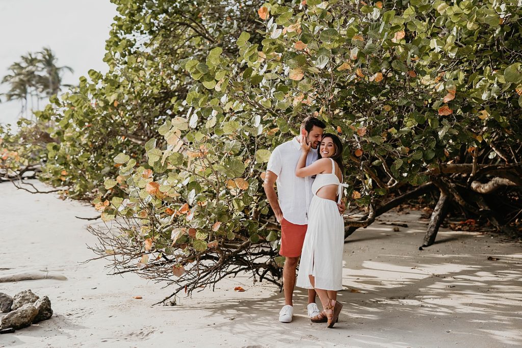 Couple holding each other and posing by beach greenery