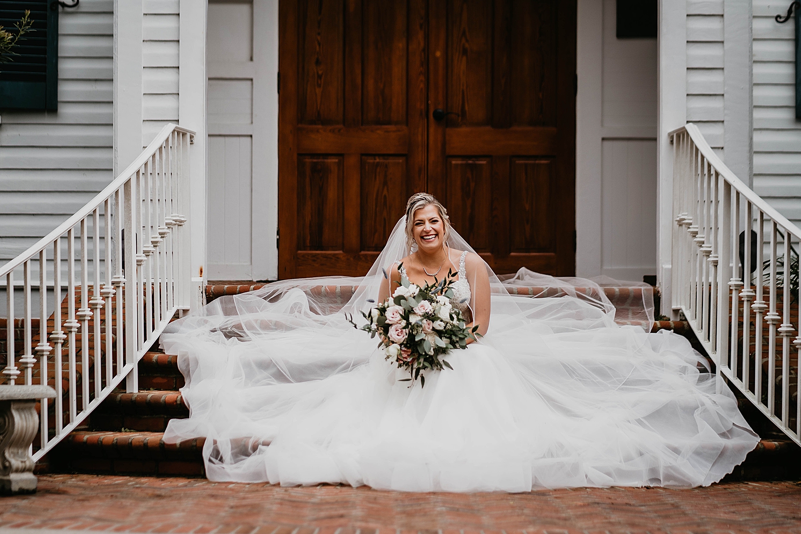 Bride sitting on house stairs with white bouquet