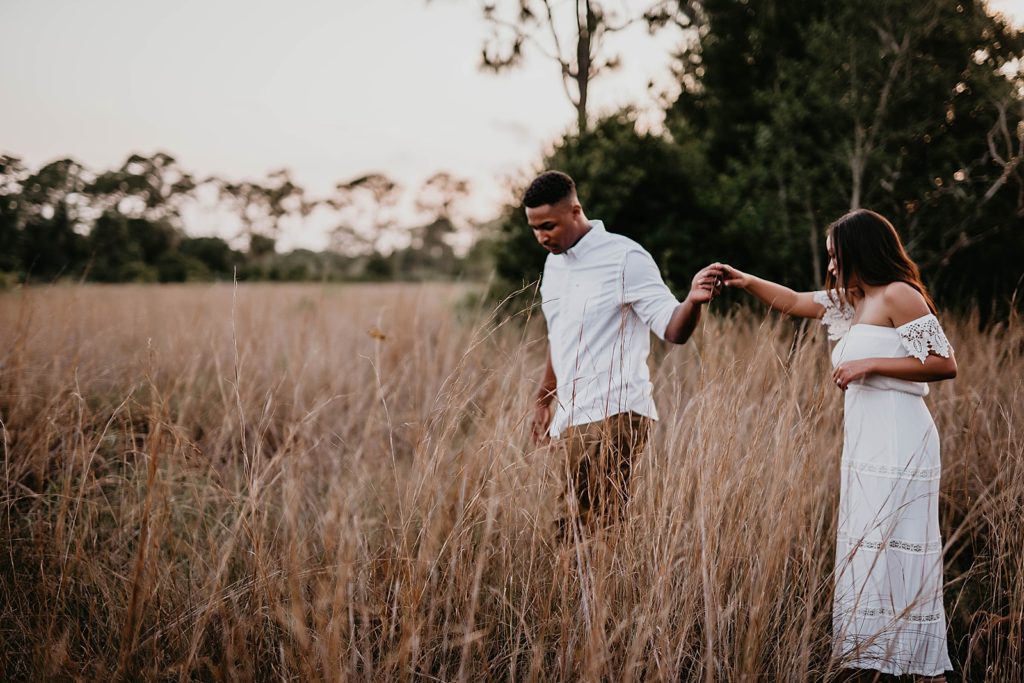 Couple holding hands navigating through tall grass field