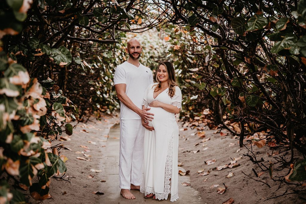 Couple standing under tree branch arch holding baby bump