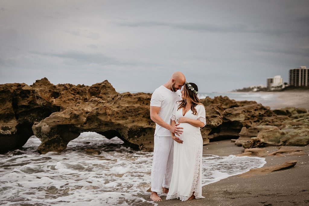 Pregnant couple standing by drift rock on the beach
