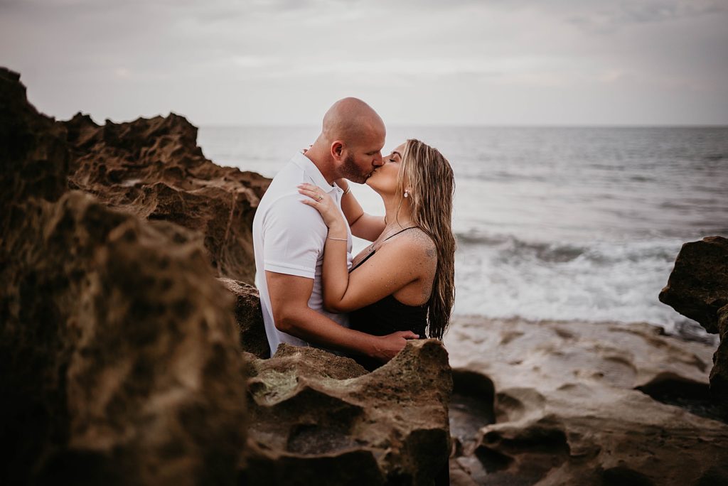 Pregnant couple kissing on the drift rocks on the beach