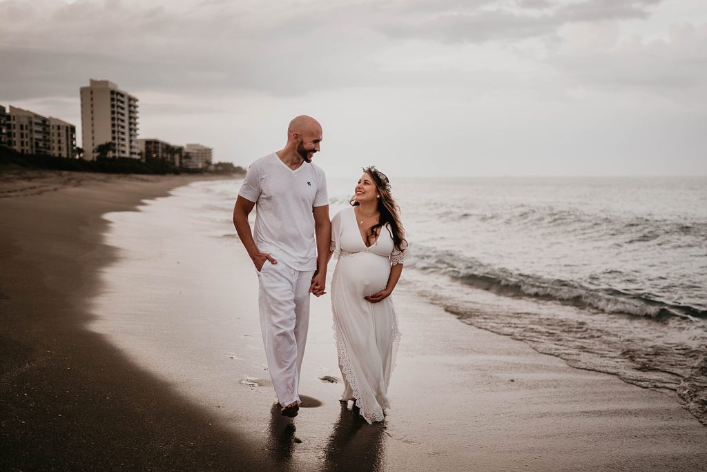 Pregnant couple holding hands and strolling on the beach