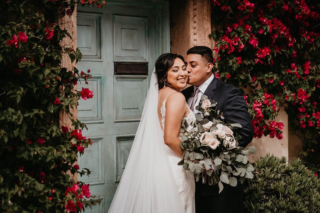 Groom kissing Bride on the cheek in front of turquoise door